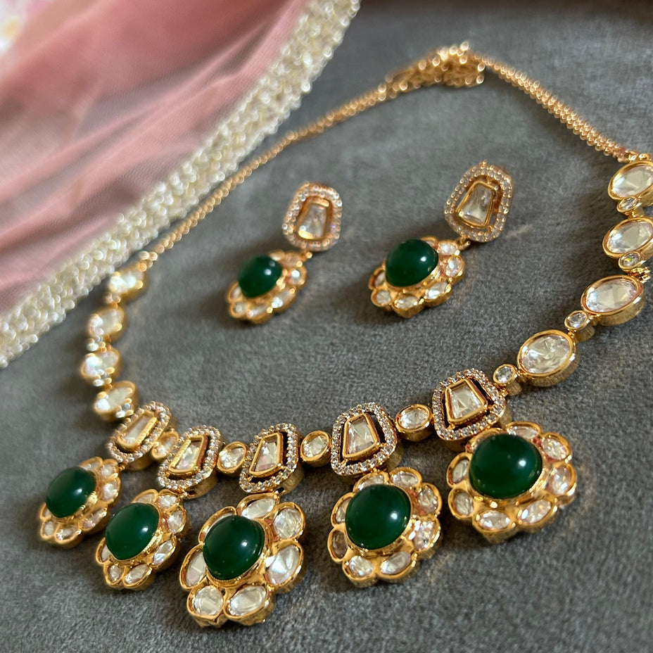Gold necklace and earrings with green gemstones on a gray surface