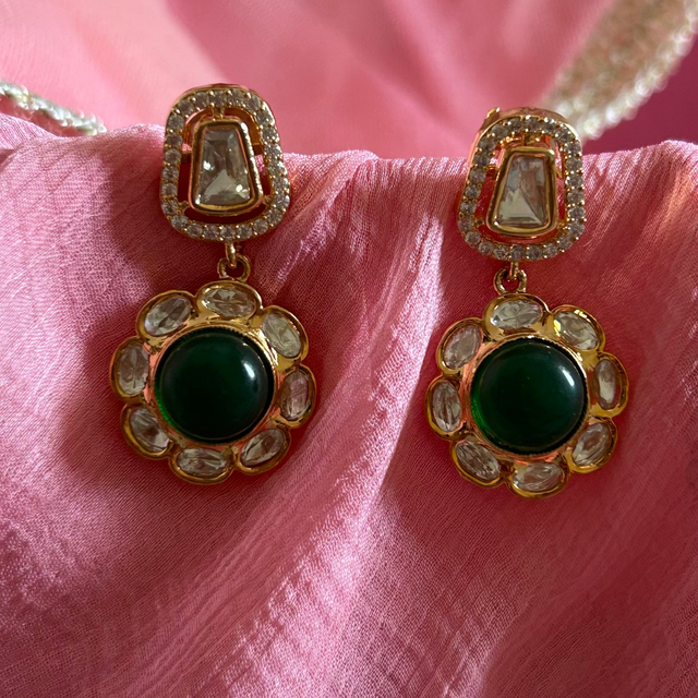 Gold earrings with green stones on a pink fabric background