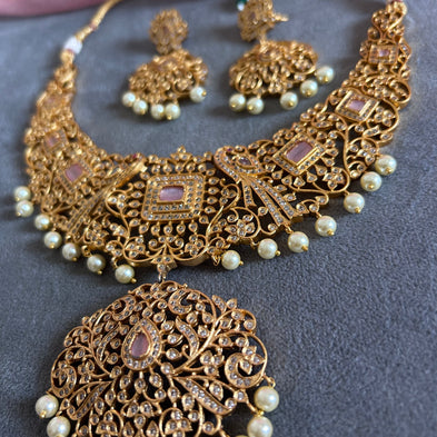 Gold necklace with pearls and matching earrings on a gray surface Gold necklace set with matching earrings on a gray surface IMITATION ARTIFICIAL ART FASHION JEWELLERY PINK STONES AD ANTIQUE PEACOCK DESIGN GOLD PLATED TEMPLE
