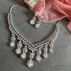 Silver necklace and earrings on a gray surface with pink fabric
