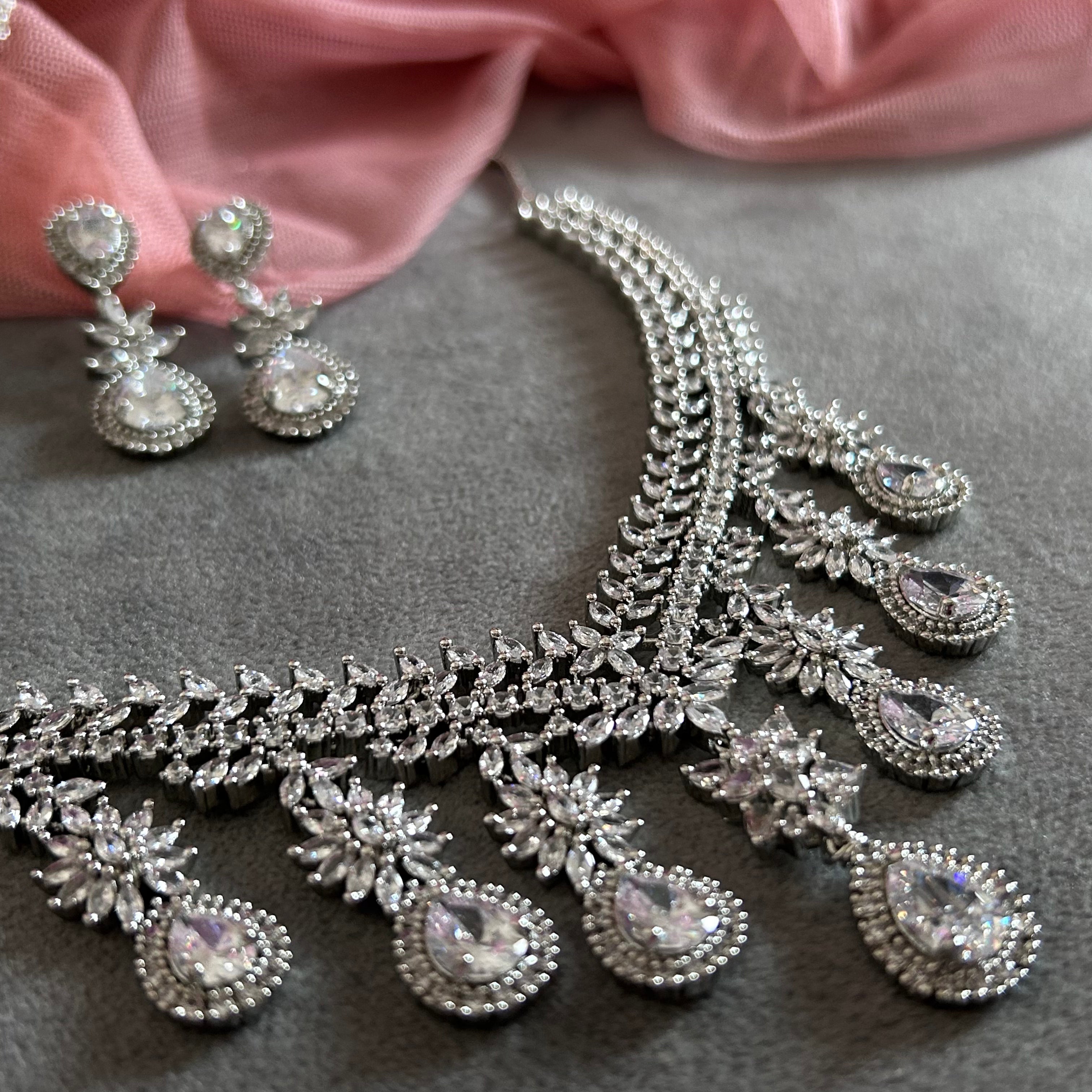 PLATINUM AMERICAN DIAMOND necklace and earrings on a gray surface with pink fabric in the background
