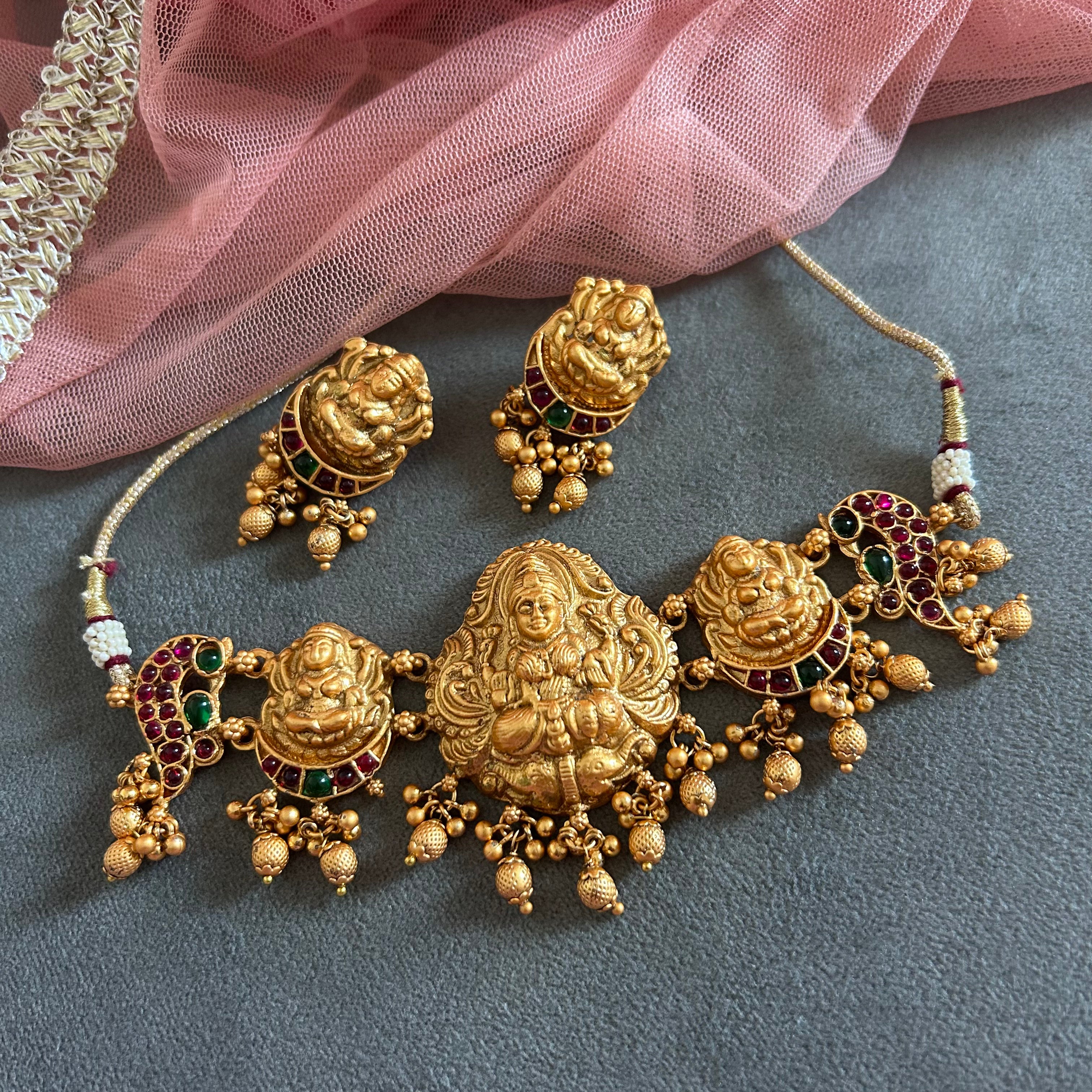 Gold necklace with intricate designs and gemstones on a gray surface with pink fabric.