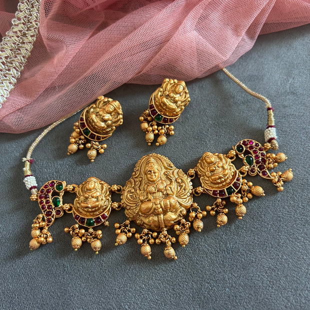 Gold necklace with intricate designs and gemstones on a gray surface with pink fabric.