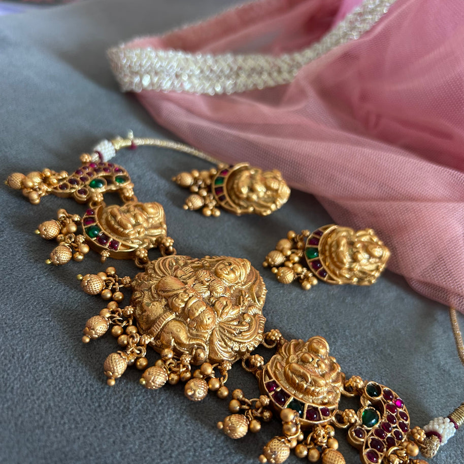 Gold jewelry set with intricate  LAKSHMI MOTIF TEMPLE designs and gemstones on a gray surface.