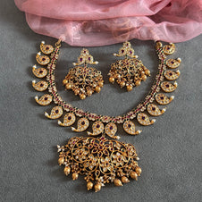 Gold necklace and earrings set on a gray surface with pink fabric in the background