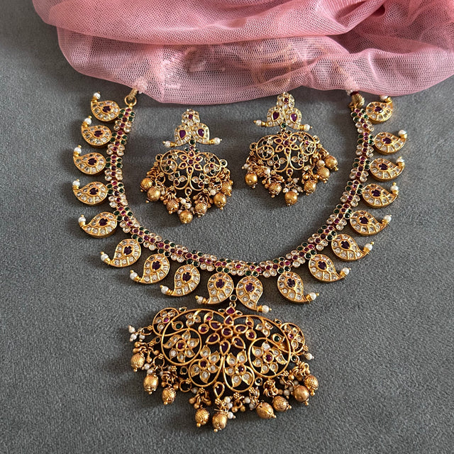 Gold necklace and earrings set on a gray surface with pink fabric in the background