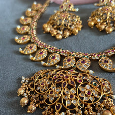 Gold necklace with intricate designs and gemstones on a gray surface