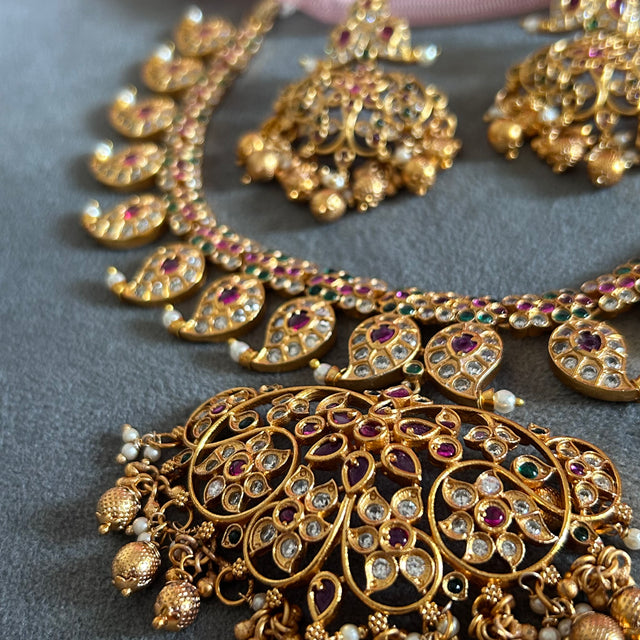 Gold necklace with intricate designs and gemstones on a gray surface