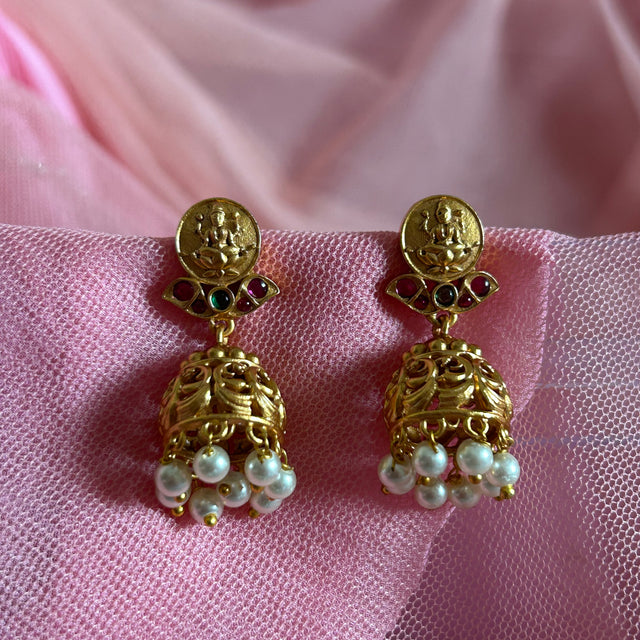Gold earrings with pearl drops on a pink fabric background