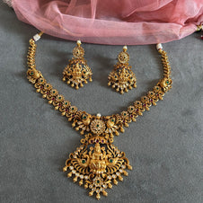 Gold necklace and earrings set on a gray surface with pink fabric in the background Gold necklace set with matching earrings on a gray surface IMITATION ARTIFICIAL ART FASHION JEWELLERY PINK STONES AD ANTIQUE PEACOCK DESIGN GOLD PLATED 