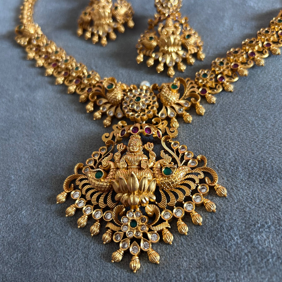 Gold necklace with intricate design on a gray background Gold necklace set with matching earrings on a gray surface IMITATION ARTIFICIAL ART FASHION JEWELLERY PINK STONES AD ANTIQUE PEACOCK DESIGN GOLD PLATED 