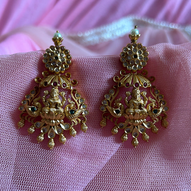 Gold earrings with intricate designs on a pink fabric background Gold necklace set with matching earrings on a gray surface IMITATION ARTIFICIAL ART FASHION JEWELLERY PINK STONES AD ANTIQUE PEACOCK DESIGN GOLD PLATED 
