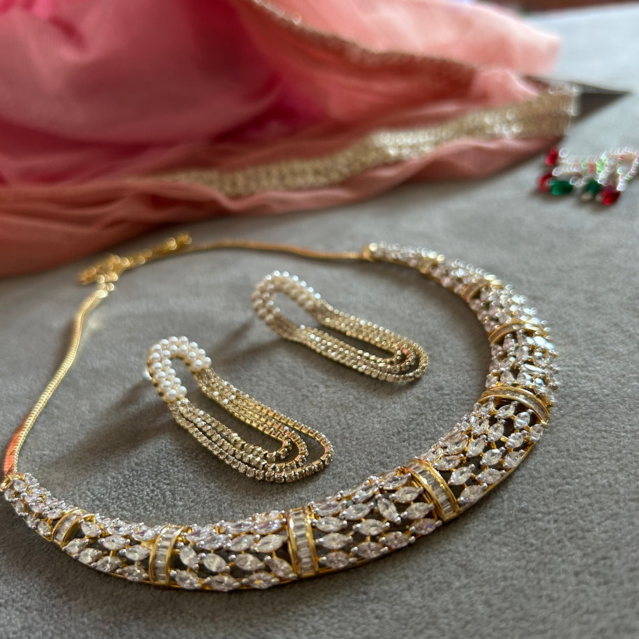 Gold and diamond necklace on a gray surface with pink fabric in the background